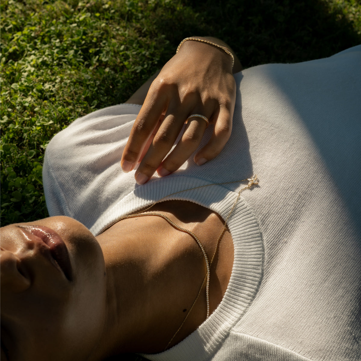 a woman resting on the grass, wearing a tennis bracelet and floral design marquise cut diamond necklace matching with a diamond eternity band and a tennis bracelet