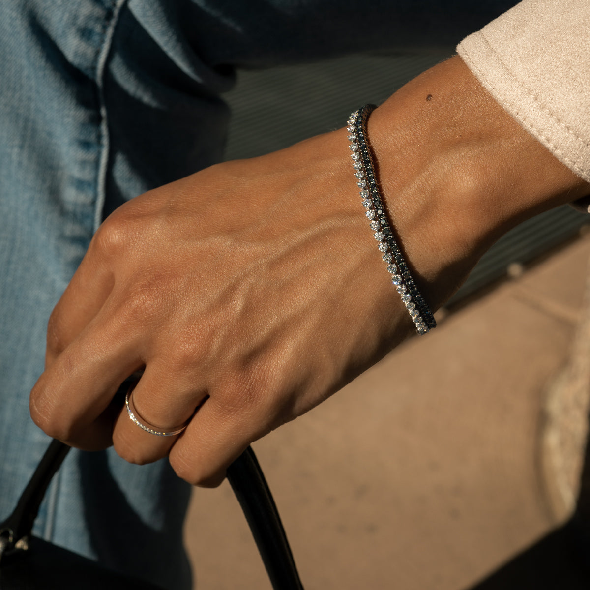 a woman wearing a 3 prong diamond tennis bracelet along with a black diamond tennis bracelet, holding a handbag