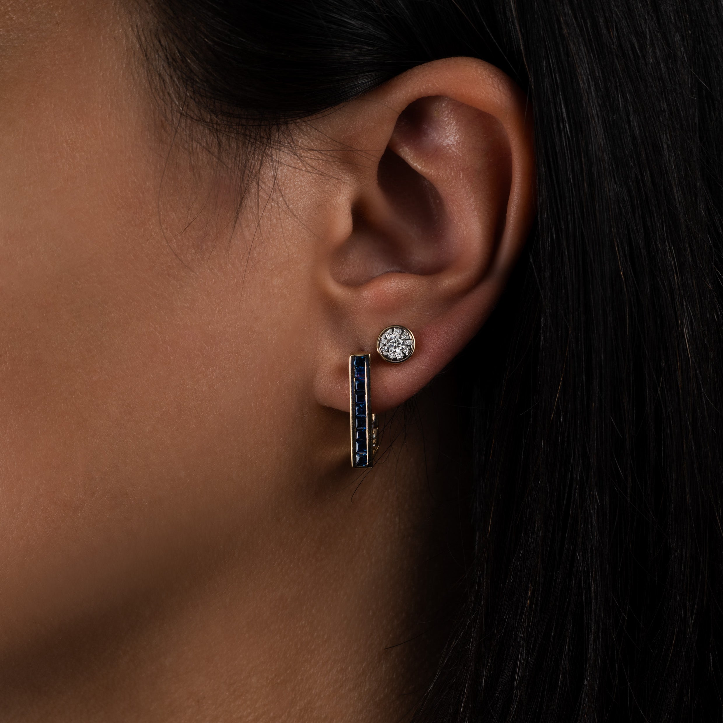 Close-up of an ear wearing a sapphire gold bar earring and a diamond stud