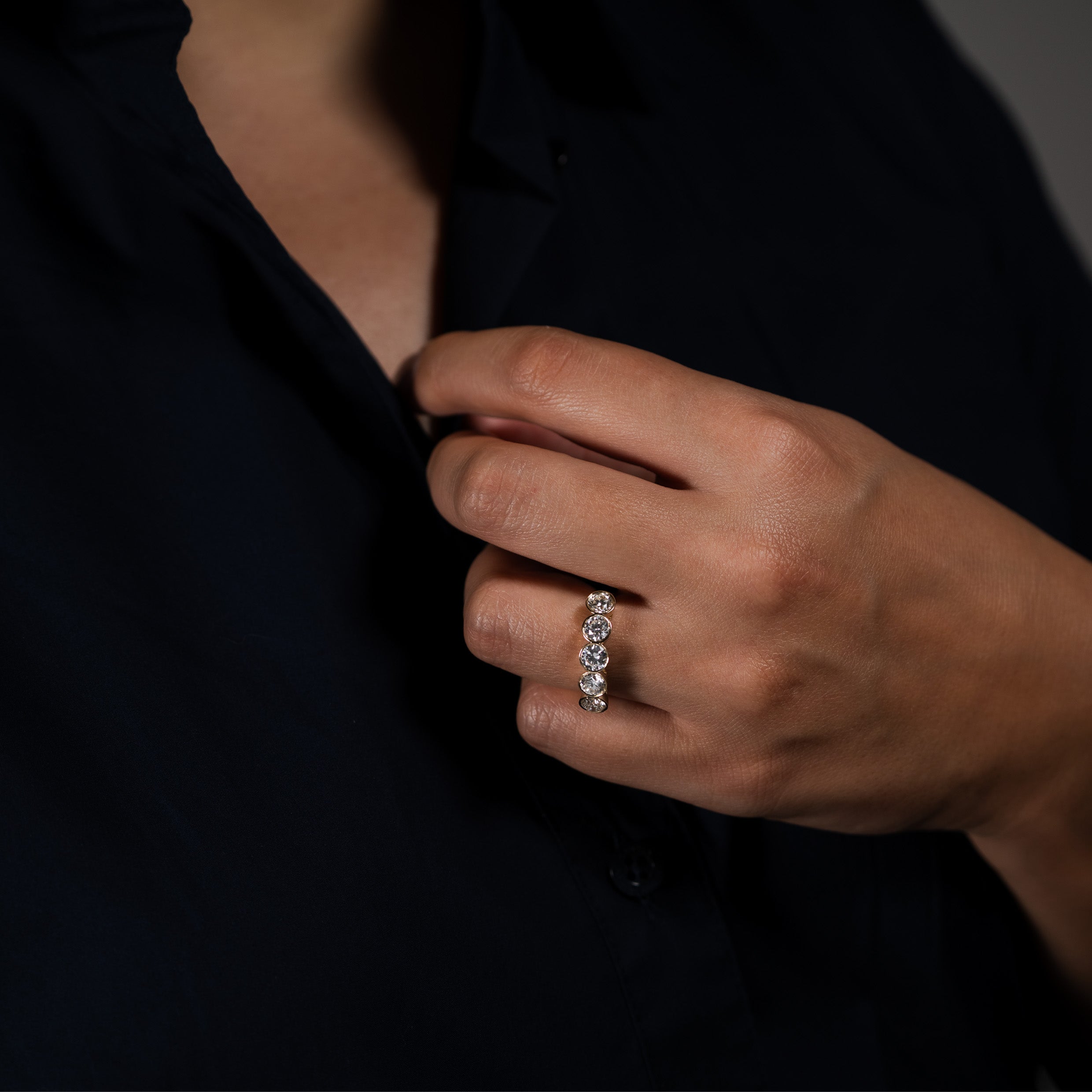 Close-up of a hand wearing a 5-stone diamond ring while buttoning a navy blue shirt.