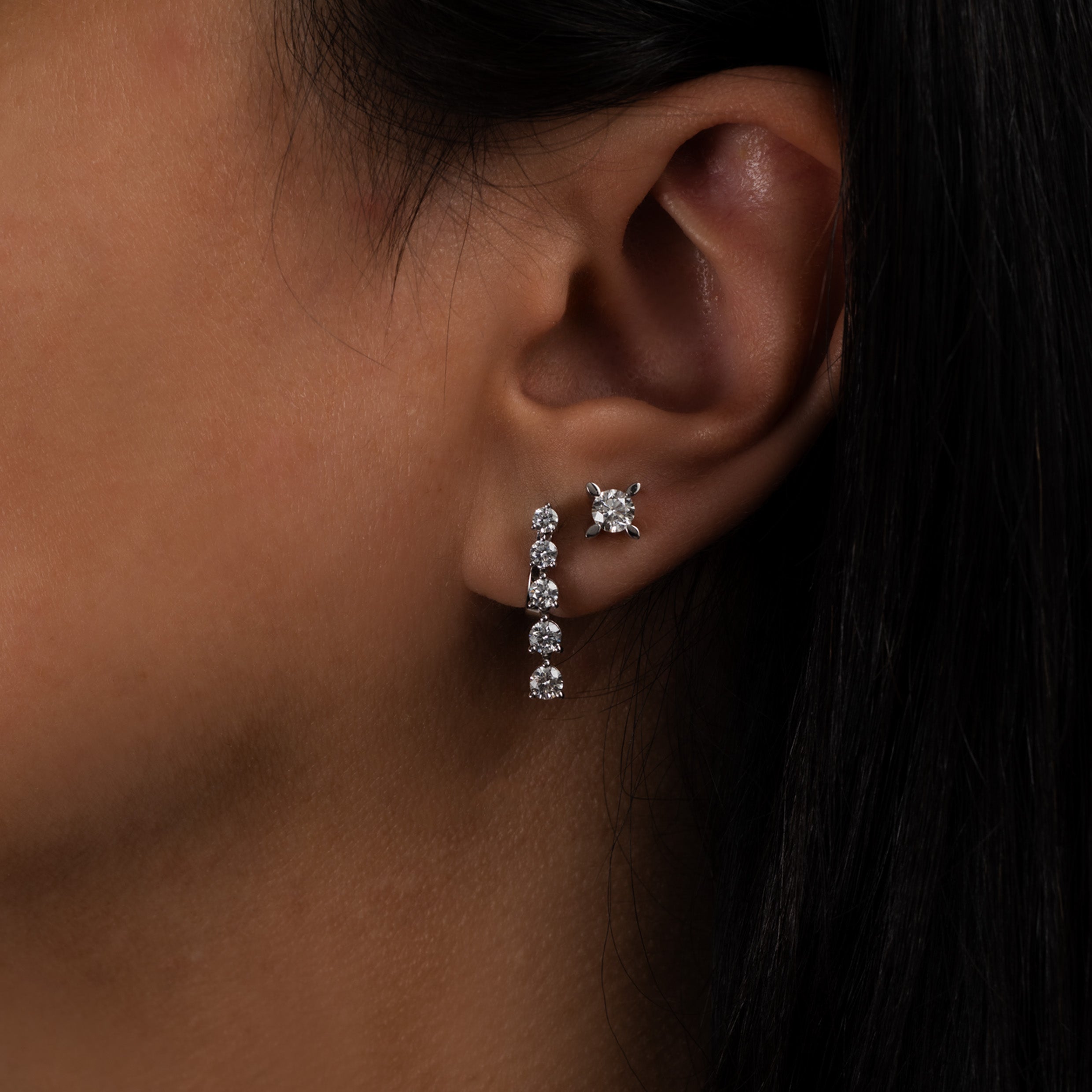 Close-up of an ear featuring a 14K white gold five-stone diamond drop earring paired with a diamond stud.