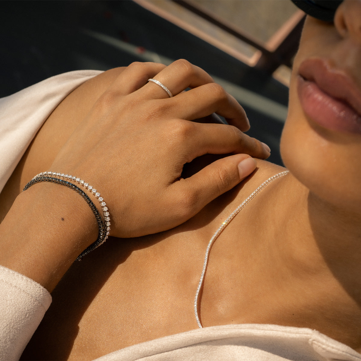 A Woman resting her wrist on her shoulder, styling with tennis bracelets and tennis necklace.