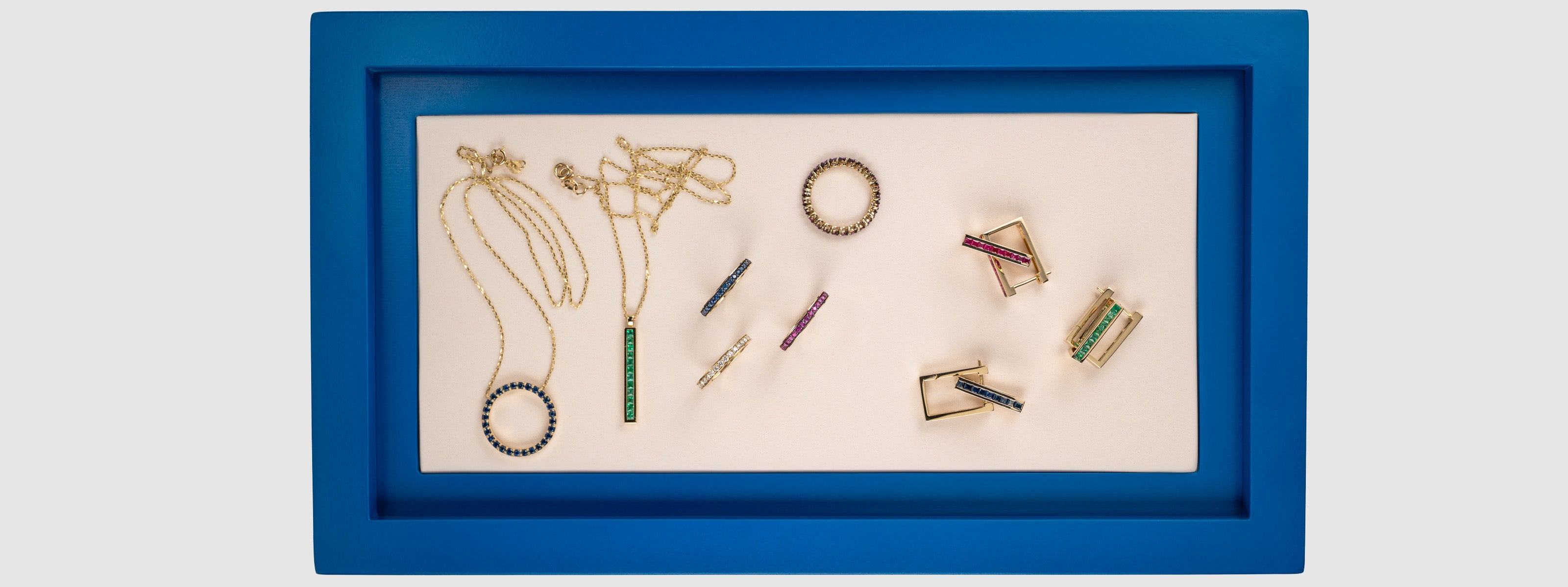 Fine jewelry collection featuring gold gemstone necklaces, rings, and earrings in a blue frame