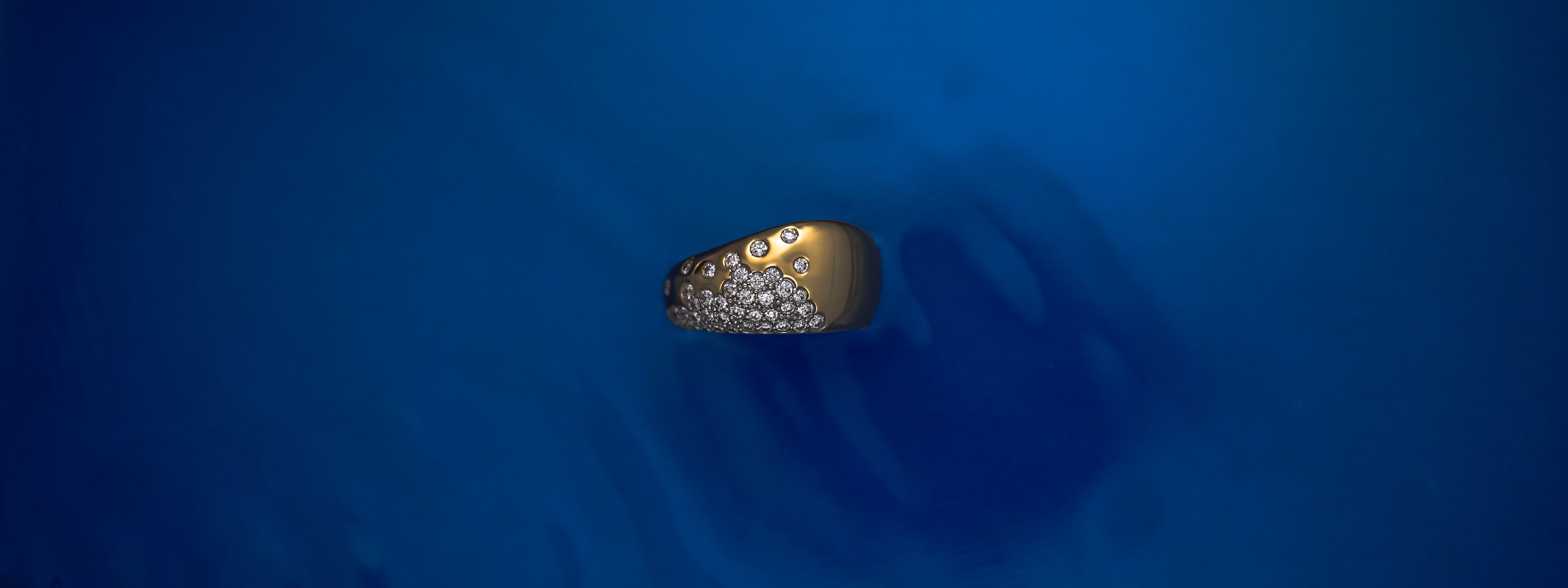 Close-up of a bold solid gold diamond ring showcased against a clean, neutral background with watery textures.