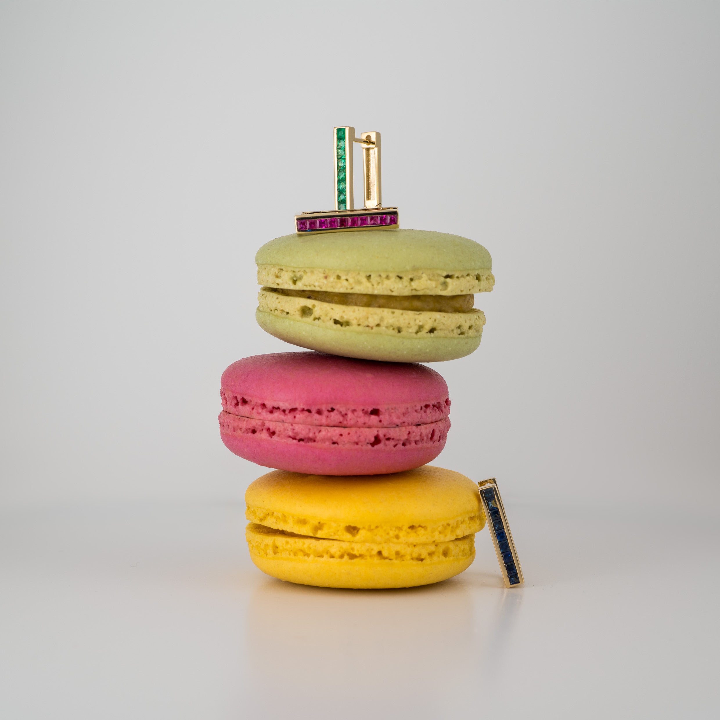 Stack of colorful macarons with gemstone earrings on top against a light gray background
