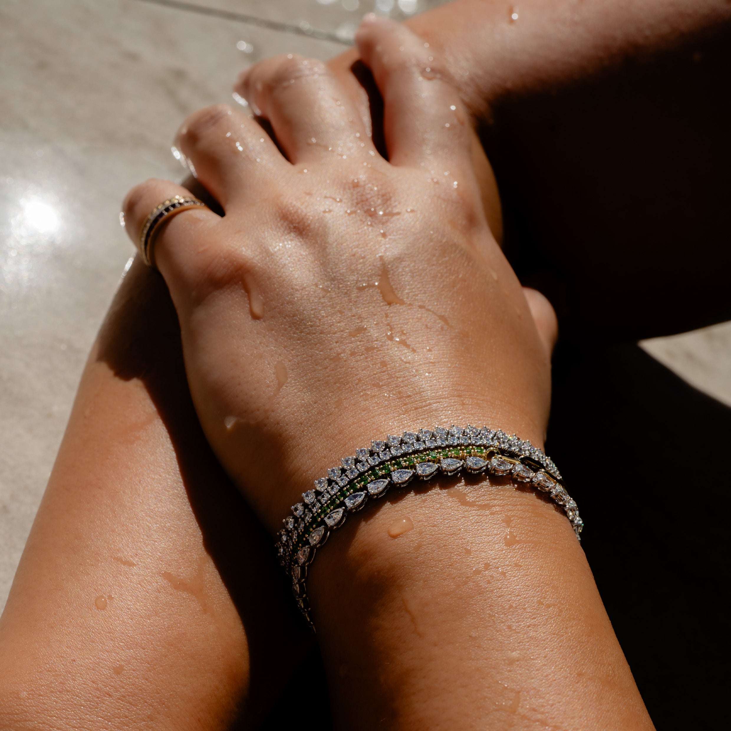 Close-up of a woman's hand wearing 14K gold diamond tennis bracelets by a pool