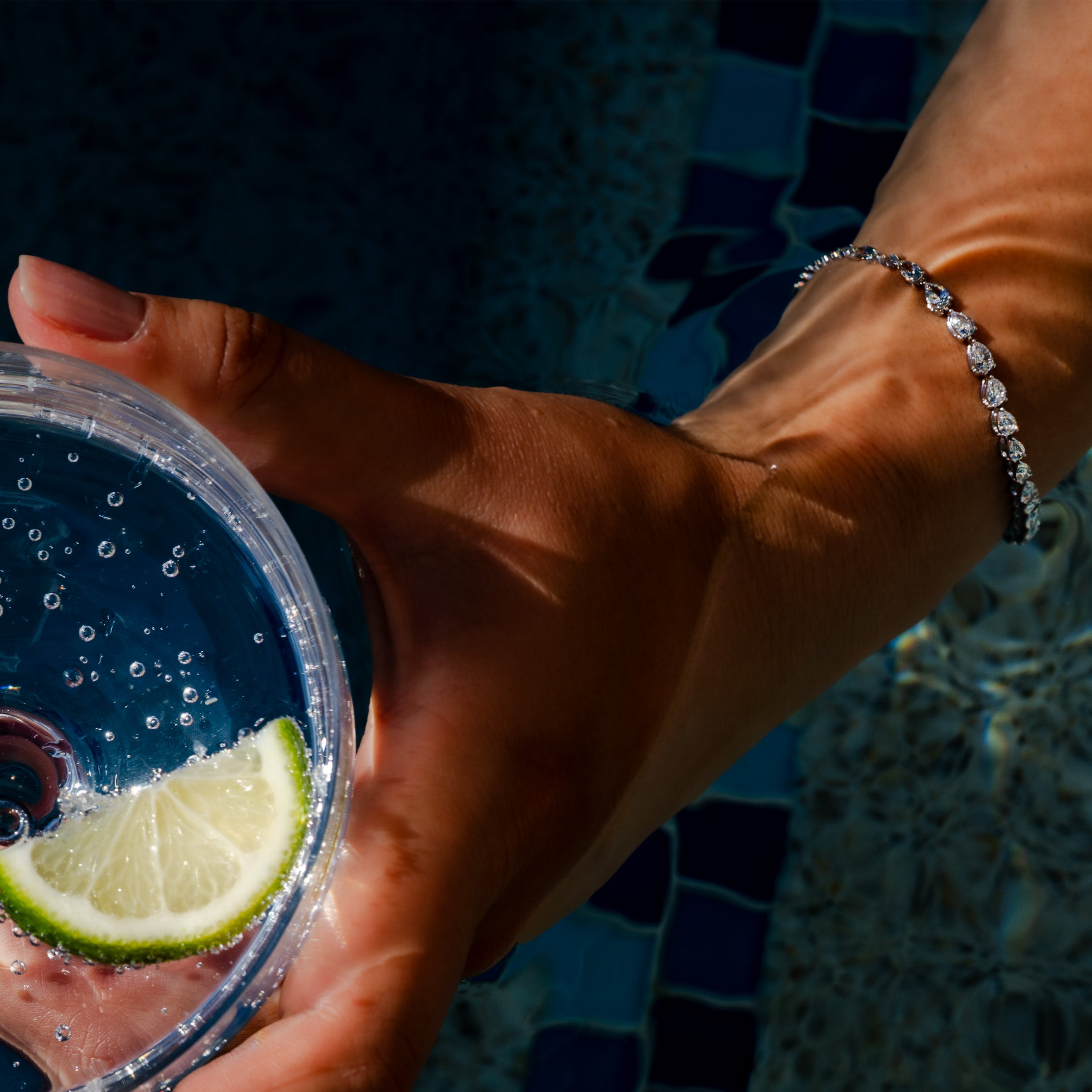 14K white gold pear cut diamond tennis bracelet on a wrist holding a drink by the pool