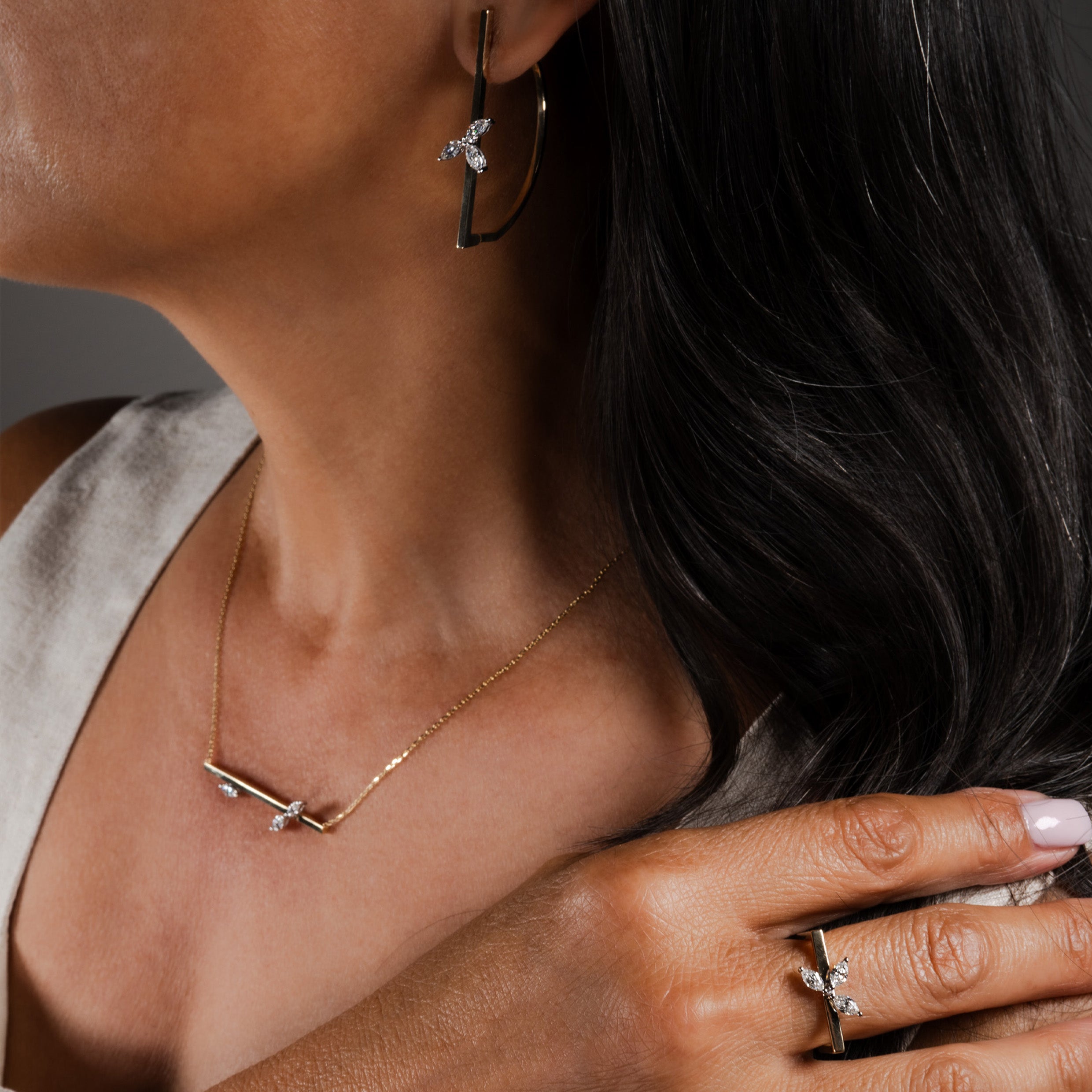 Close-up of a model wearing a 14K gold marquise diamond-cut earring, necklace, and ring set against a neutral background.
