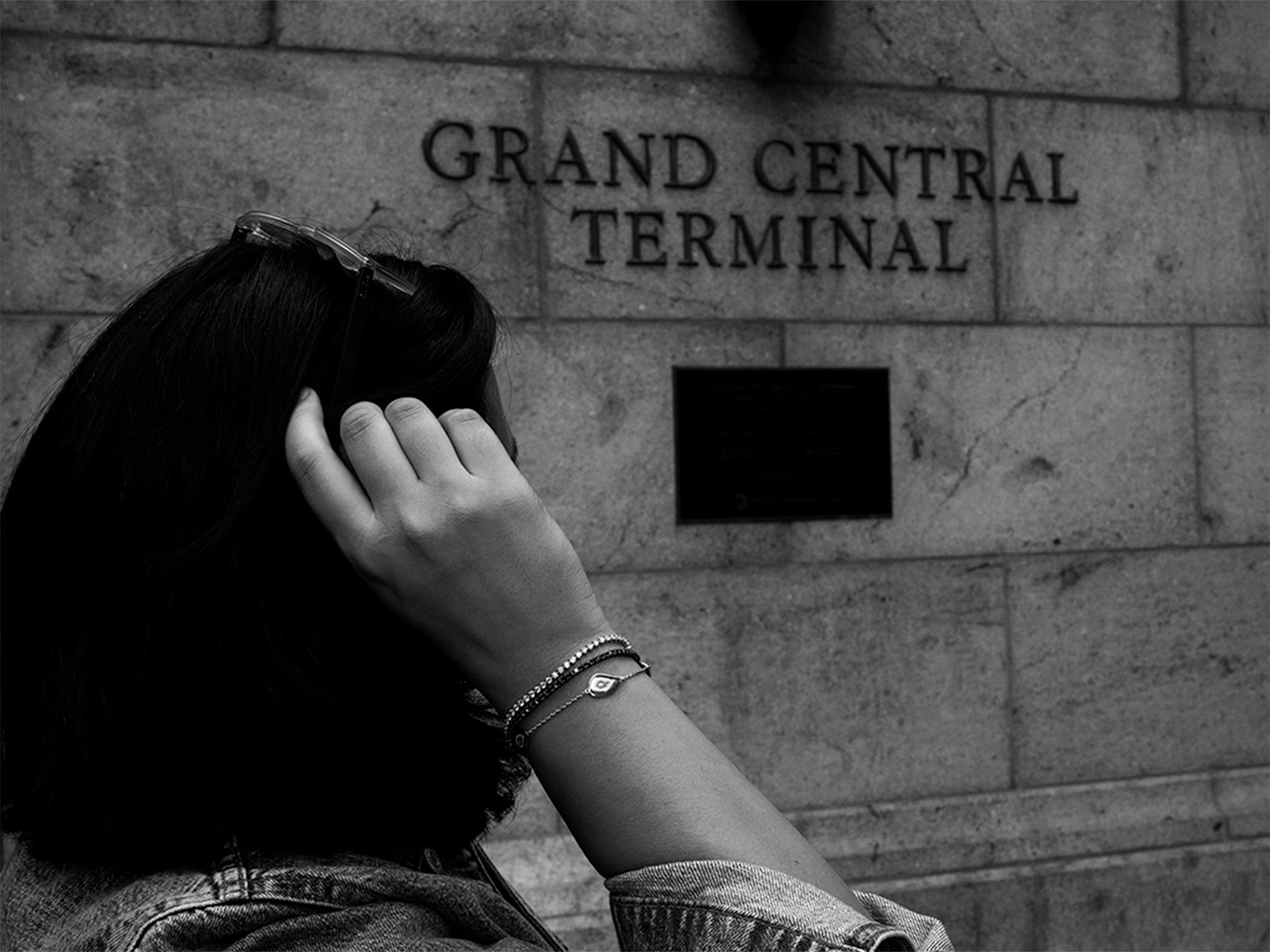 Person with hand on head wearing diamond bracelets in front of 'Grand Central Terminal' sign