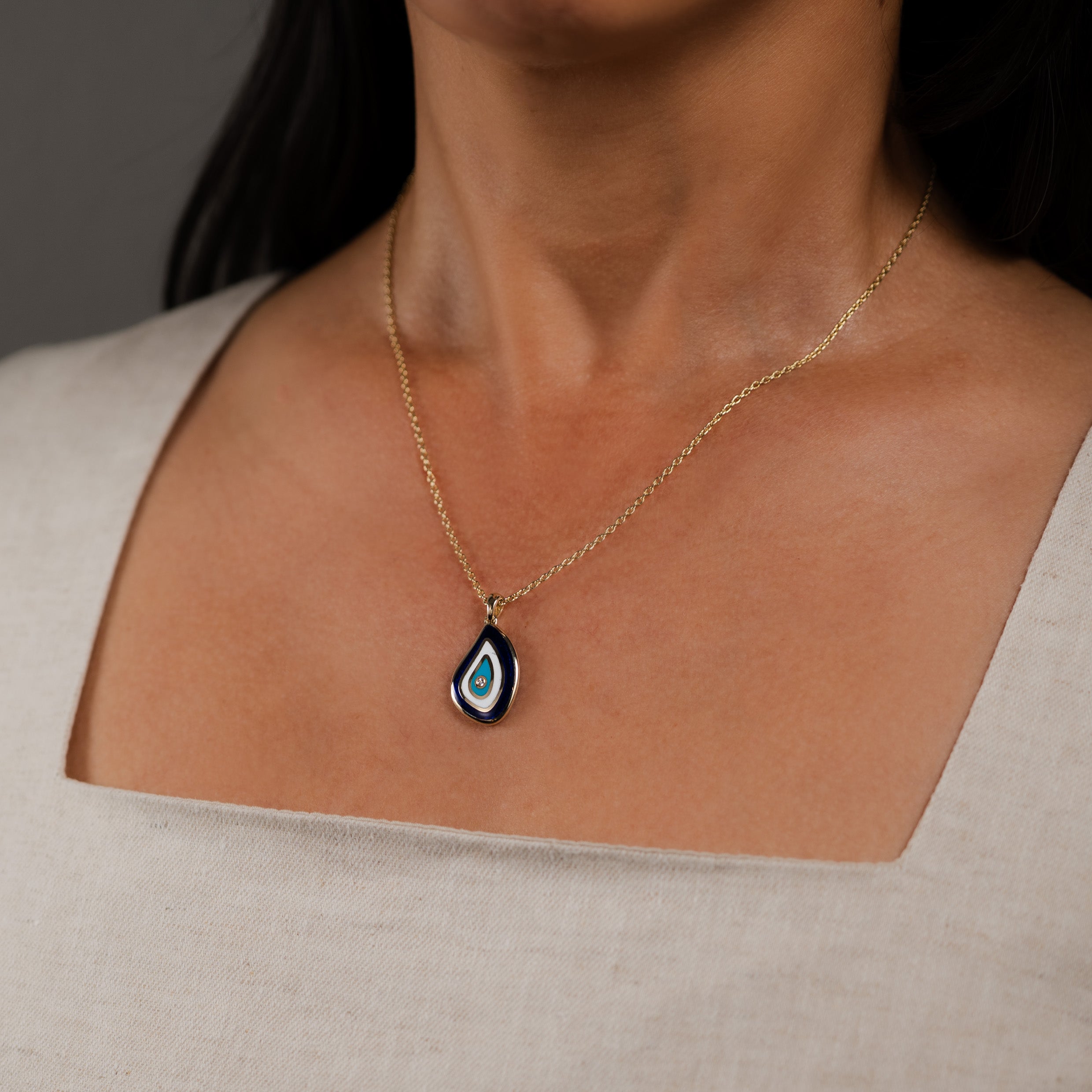 Necklace with a teardrop-shaped evil eye pendant worn by a person against a neutral background