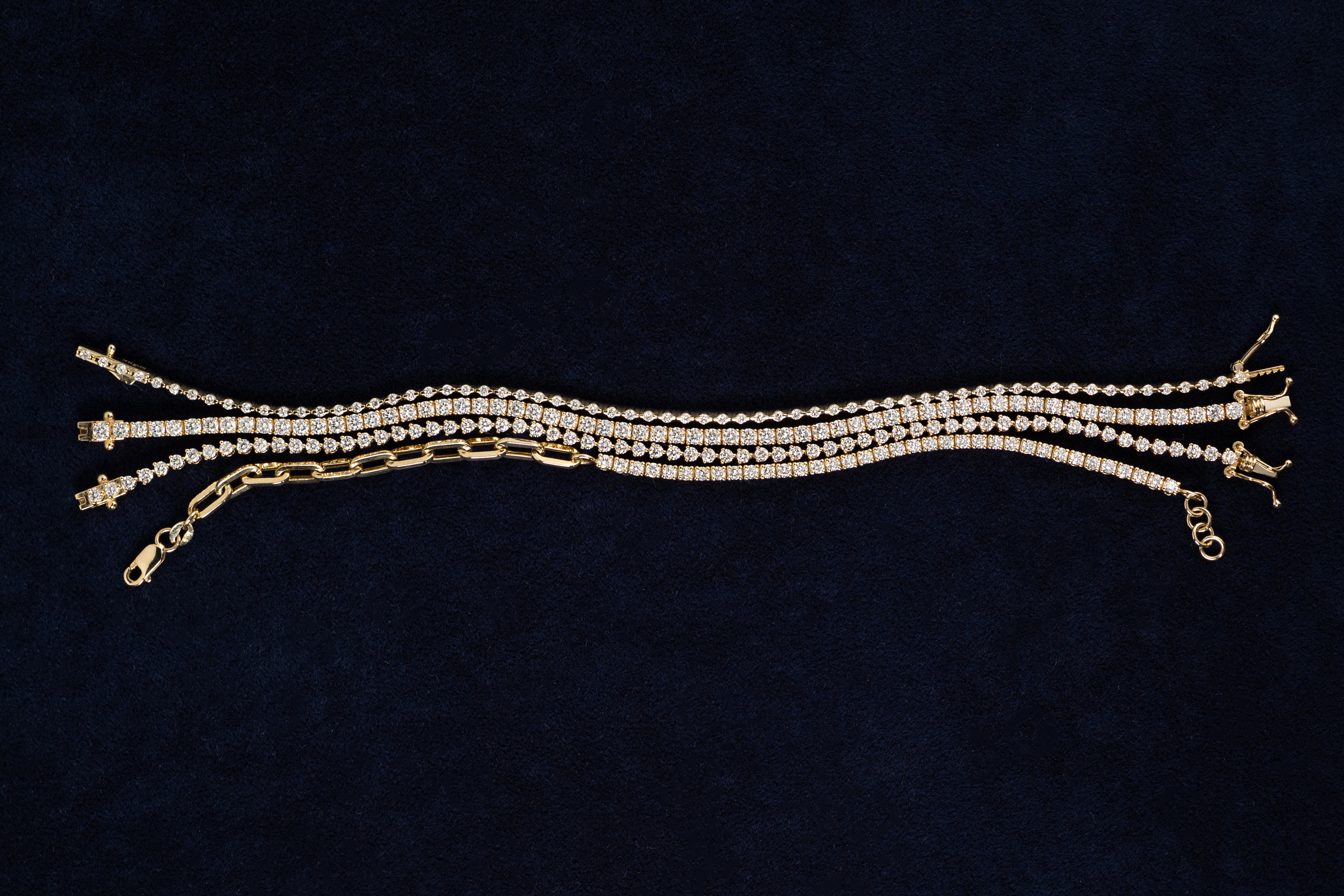 Gold and diamond tennis bracelets on a dark blue velvet background