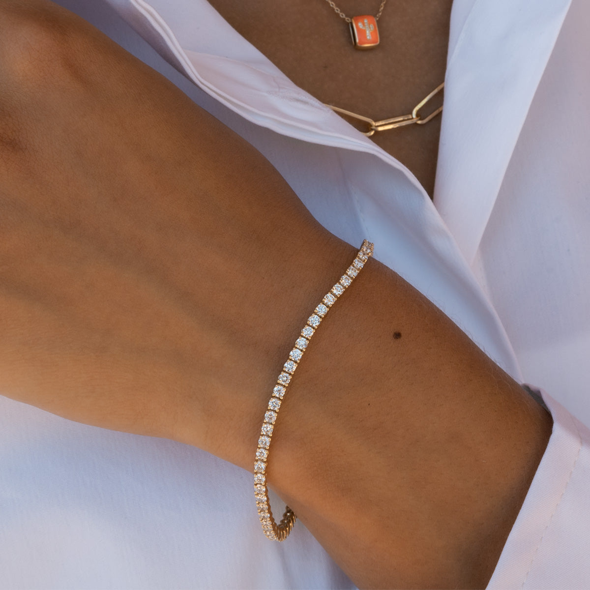 A close-up of a person's hand resting on her shoulder, wearing a diamond tennis bracelets on the wrist