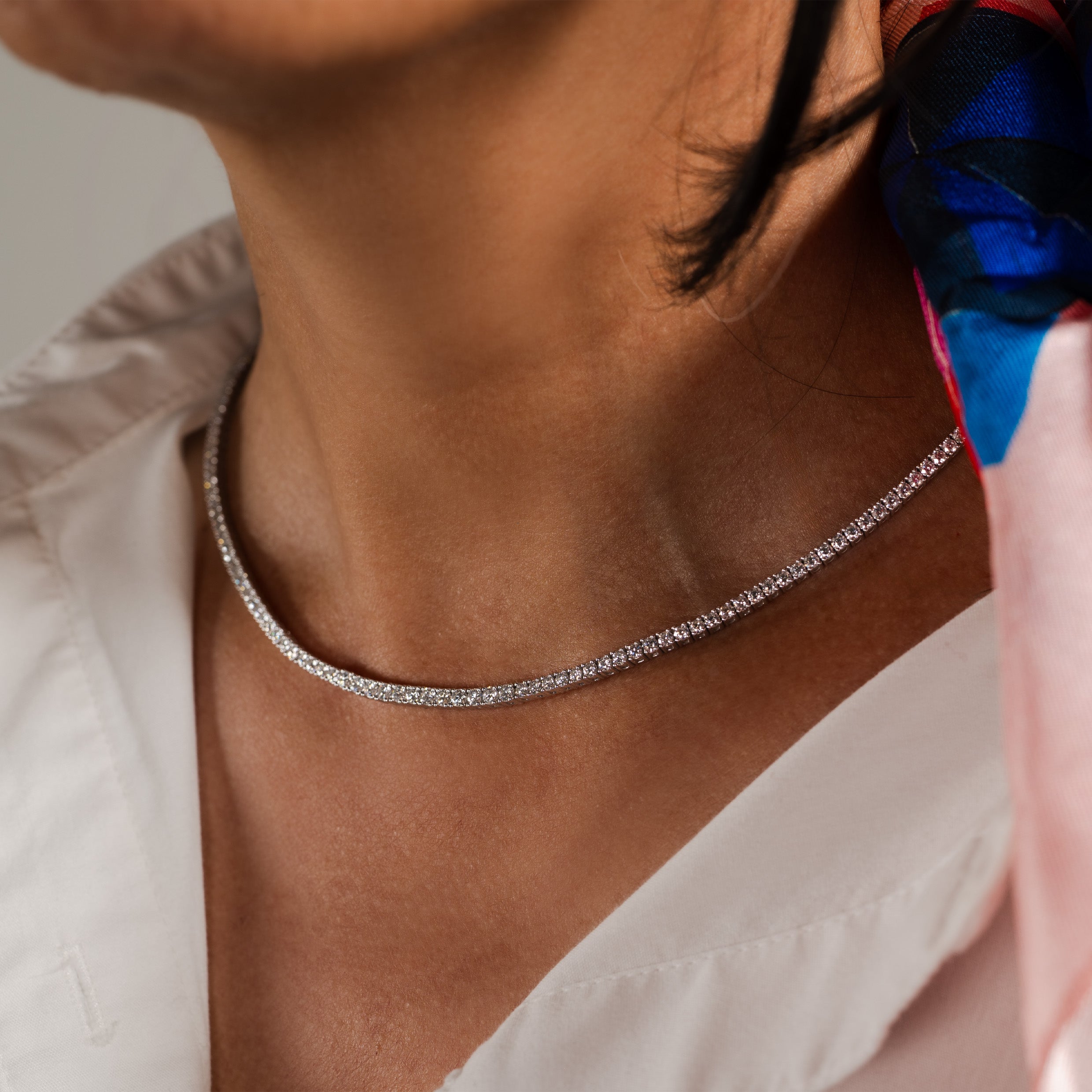 Close-up of a model wearing a 4-prong diamond tennis necklace against a soft, neutral background.