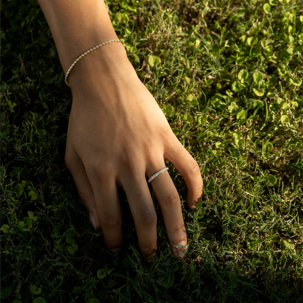 a woman's hand resting on the grass, wearing a thin tennis bracelet and a eternity band