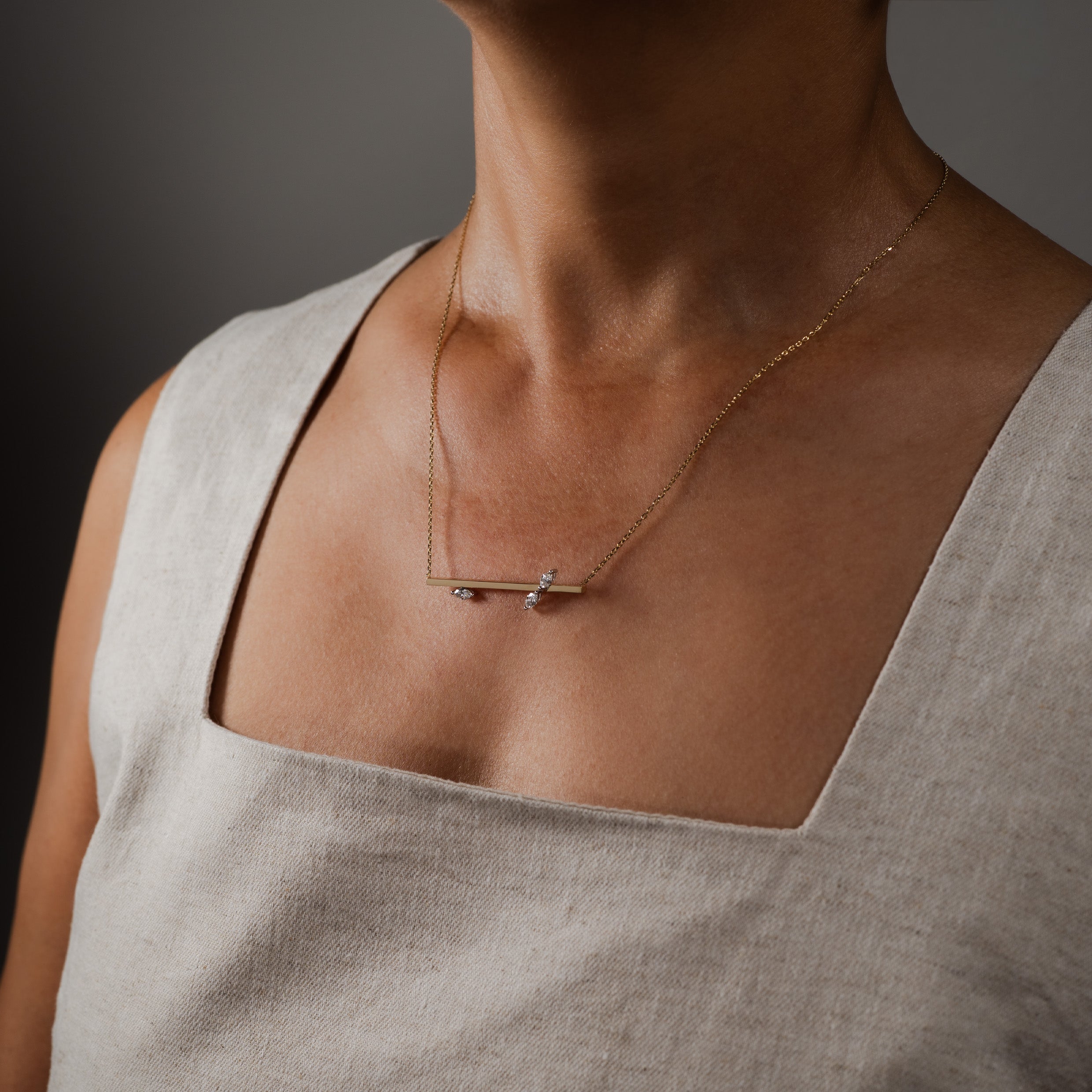 Solid gold necklace featuring a marquise-cut diamond pendant, worn by a model in a light-colored linen top against a dark, contrasting background.