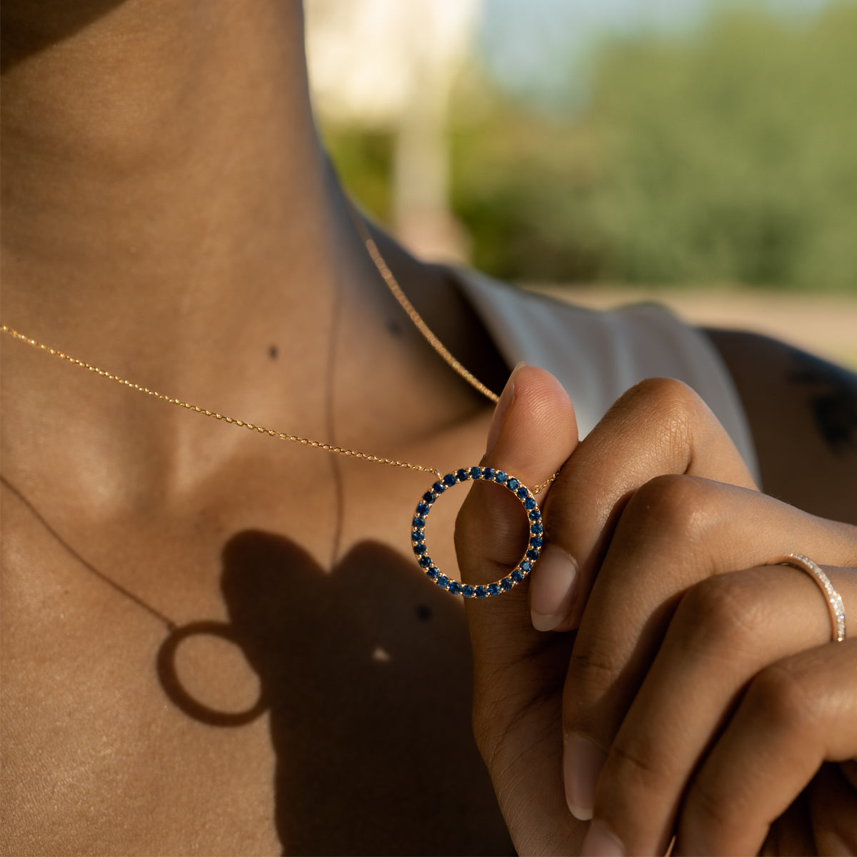 a woman holding a gold chain around her neck with a 14K yellow gold princess cut blue sapphire circular pendant