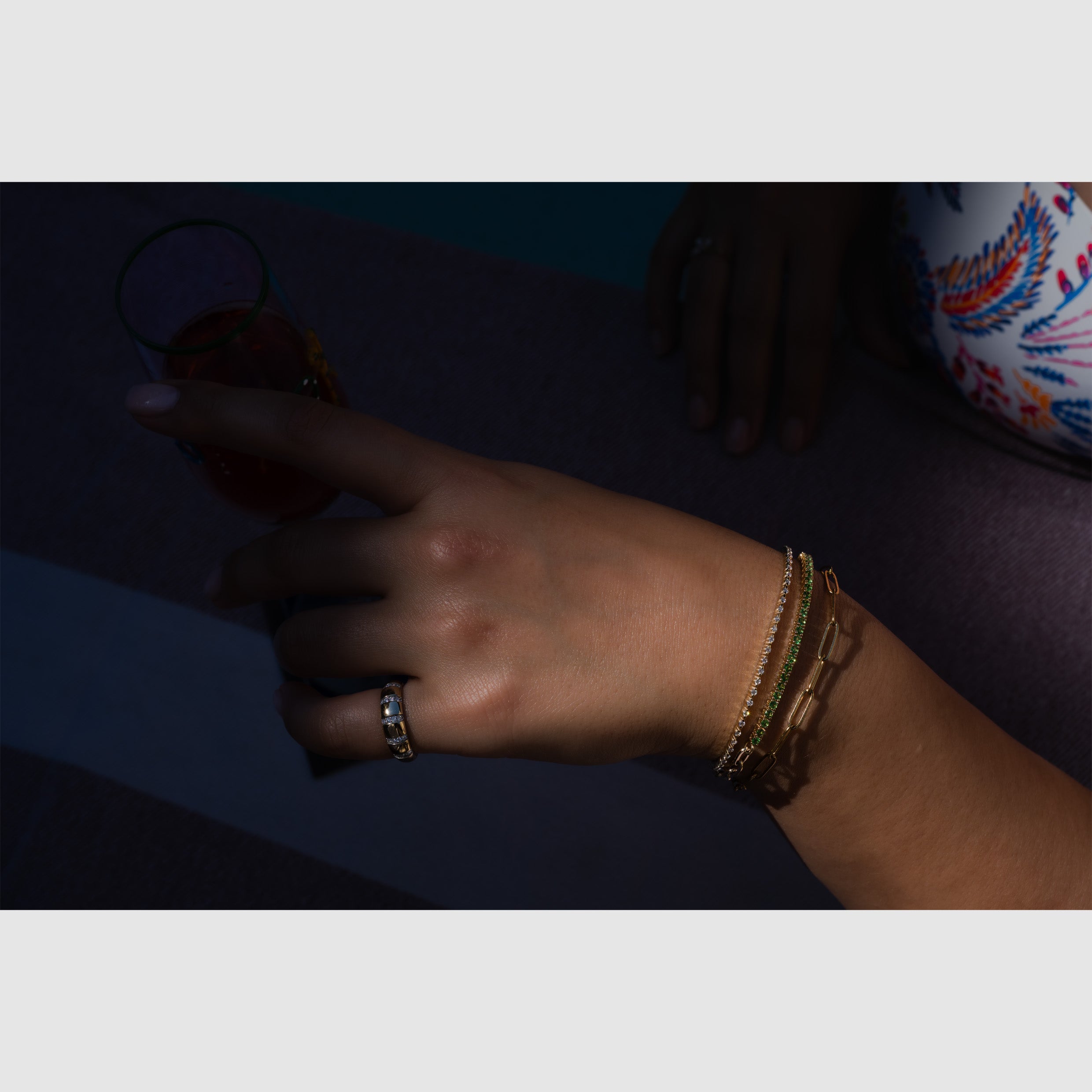 Hand wearing a gold diamond statement ring and tennis bracelets, captured poolside with a blurred background.