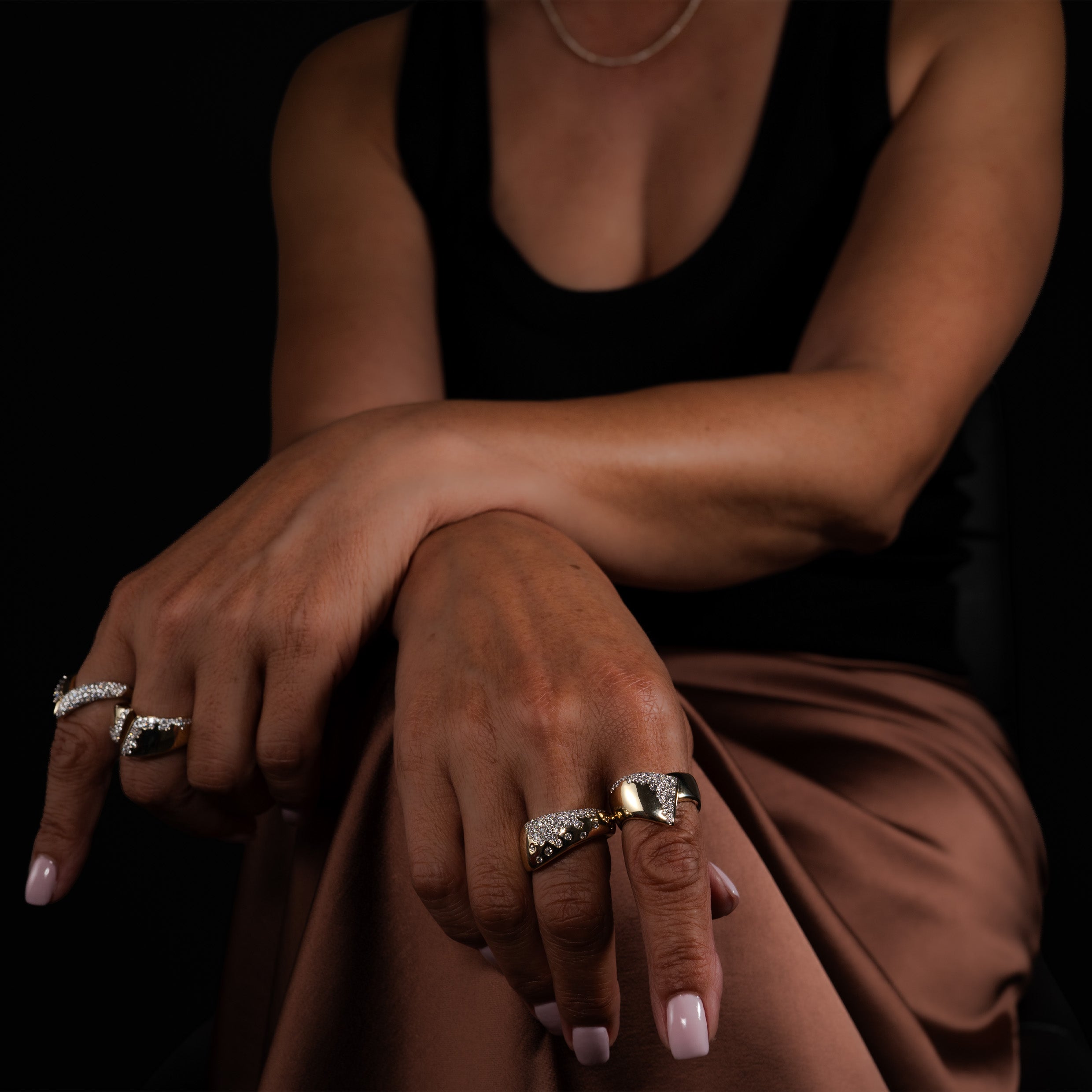Close-up of a model wearing bold gold and diamond rings, showcased against a dark background.