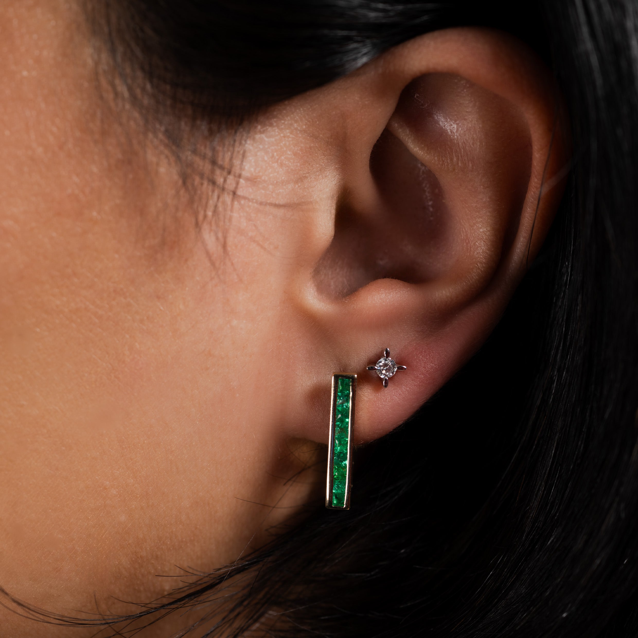 Close-up of an ear wearing an emerald gold bar earring and a diamond stud.