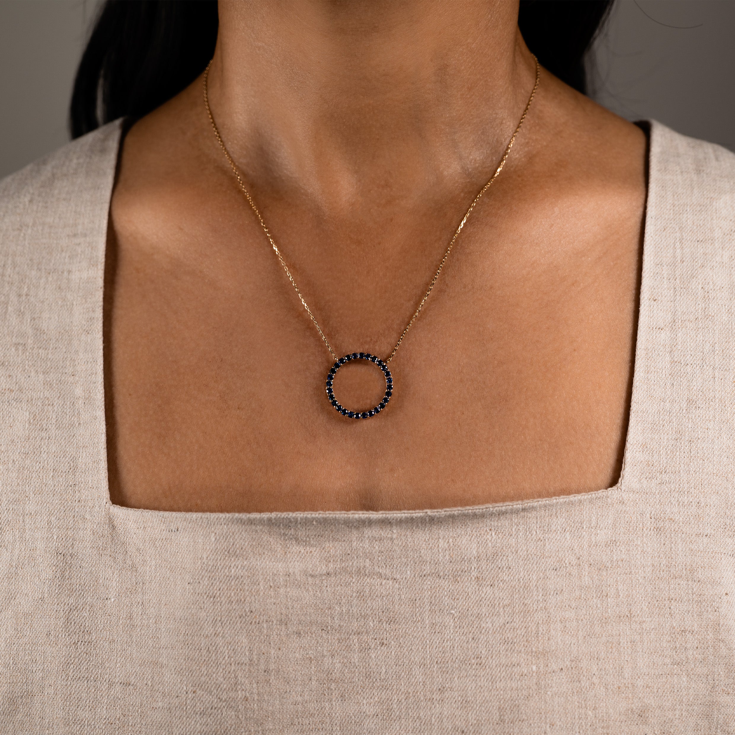 Necklace with a blue sapphire circular pendant worn by a model against a neutral background
