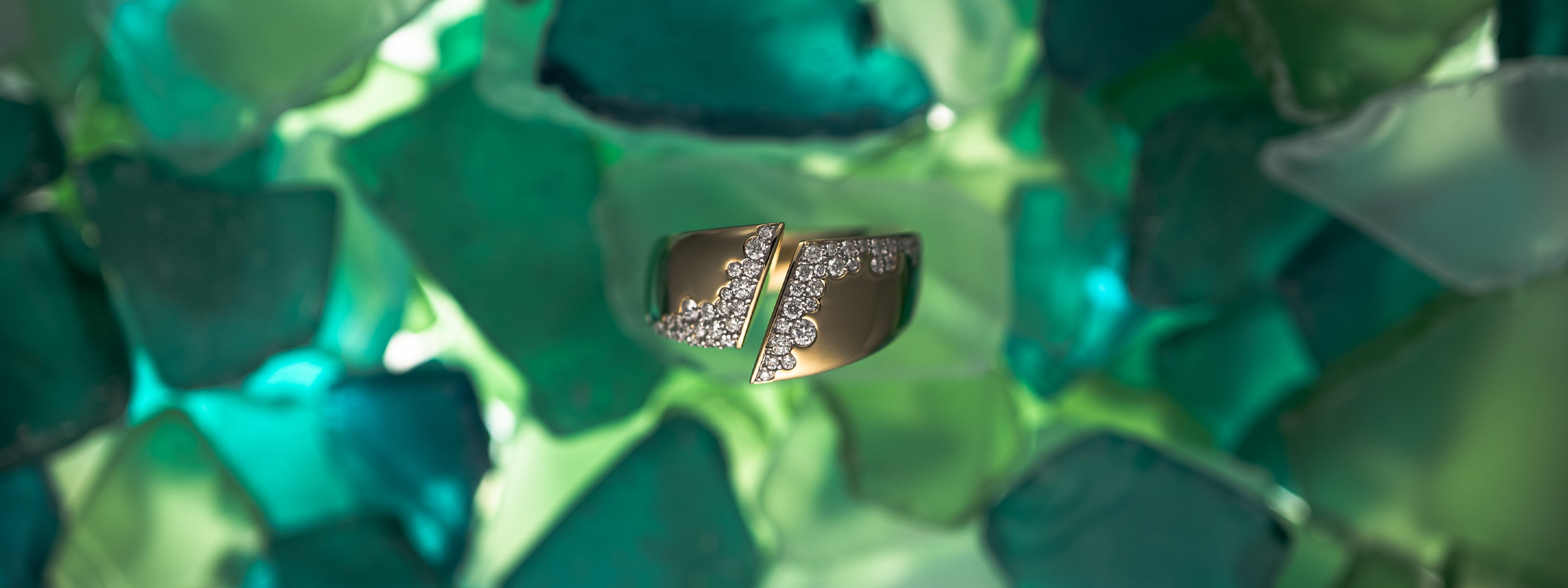 Close-up of a bold solid gold diamond ring showcased against a backdrop of decorative green glass fragments.