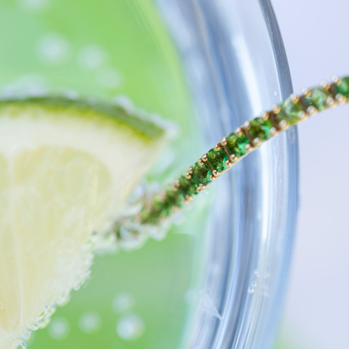 a close up photo of a green garnet tennis bracelet in a cocktail glass