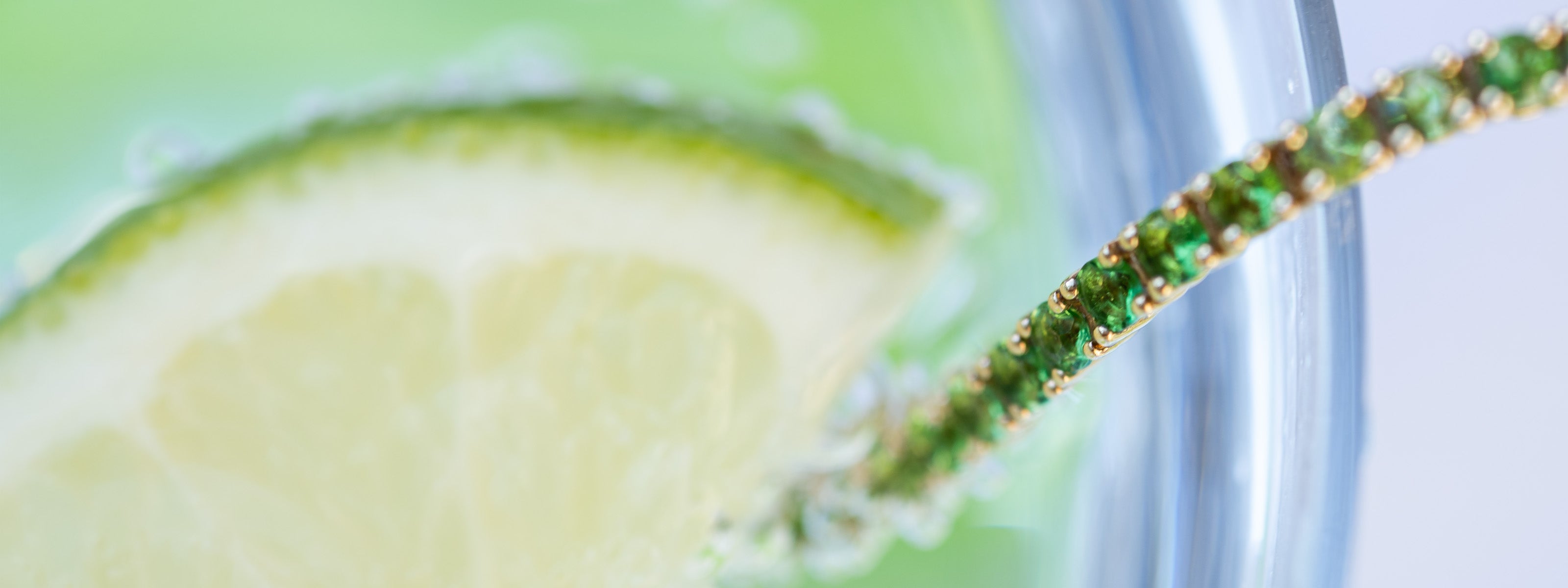 Close-up of a green garnet tennis bracelet in a glass of soda with lime