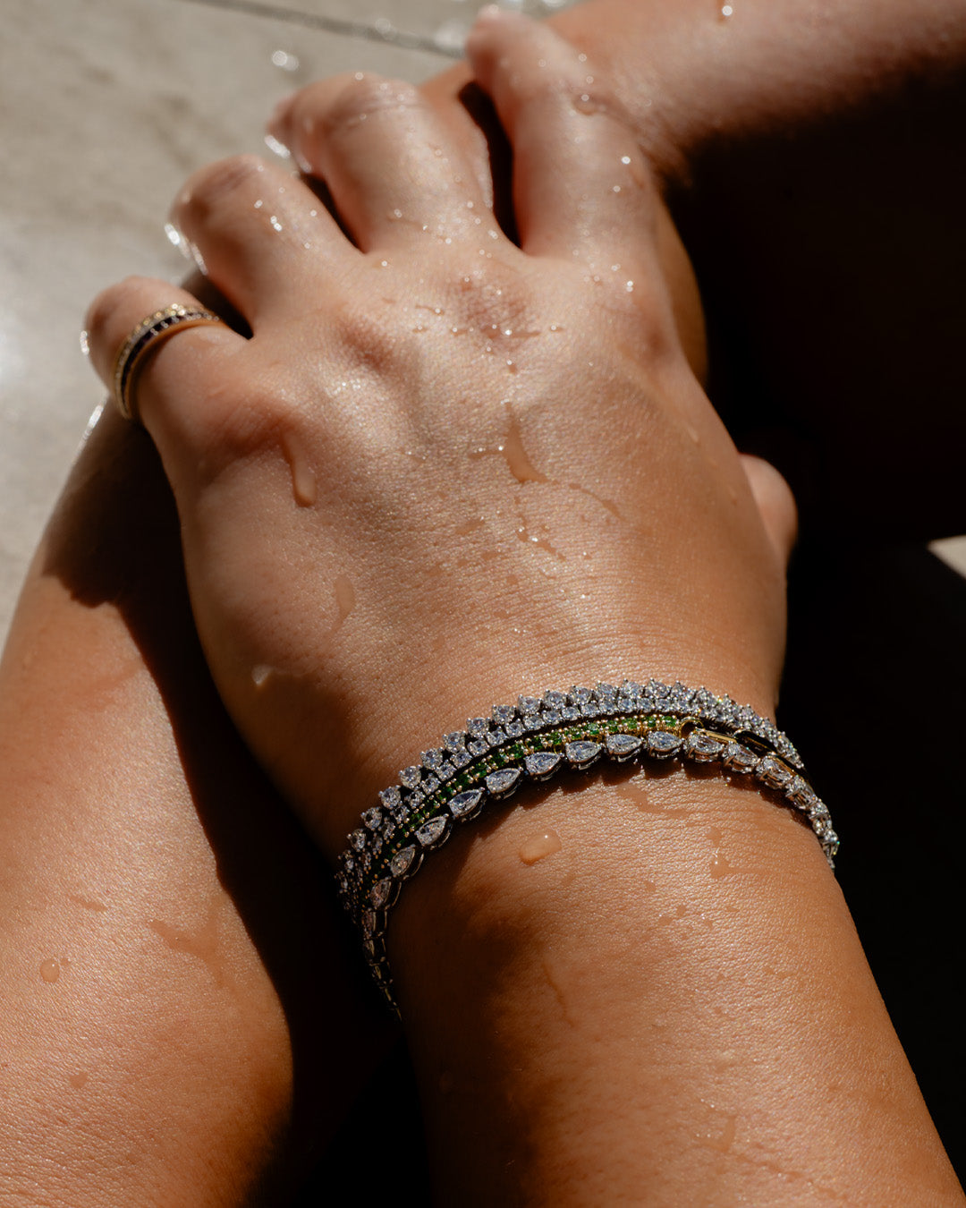 Close-up of a woman's hand wearing 14K gold diamond tennis bracelets by a pool