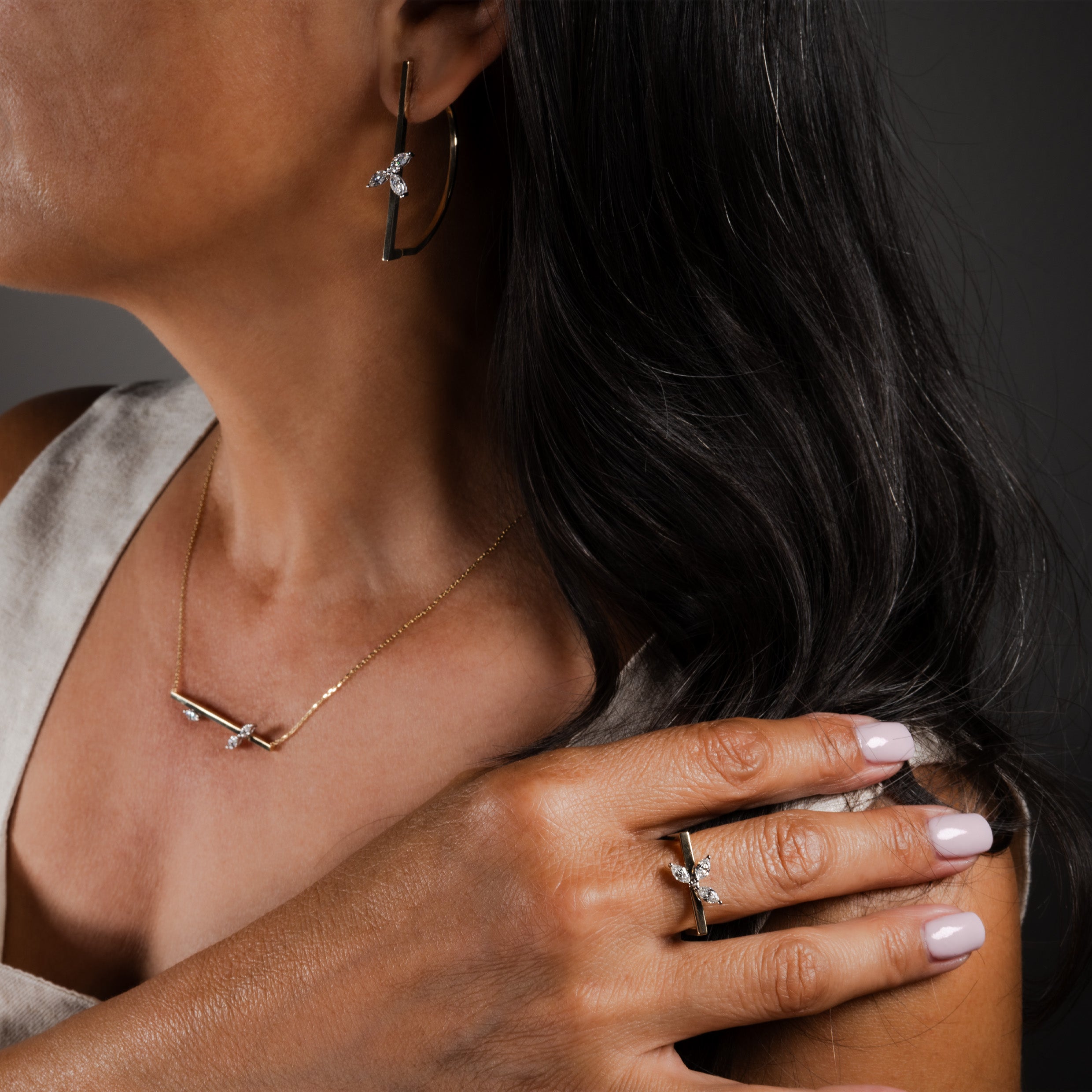 Close-up of a model wearing a 14K gold marquise diamond-cut earring, necklace, and ring set against a neutral background.