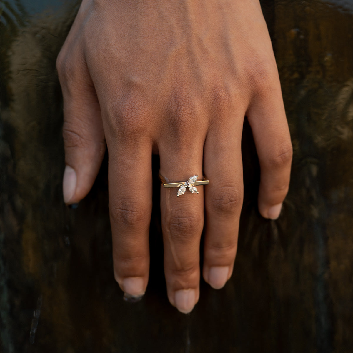 a close up photo of a hand wearing a gold ring with a geometric frame and three marquise-cut clear diamonds 