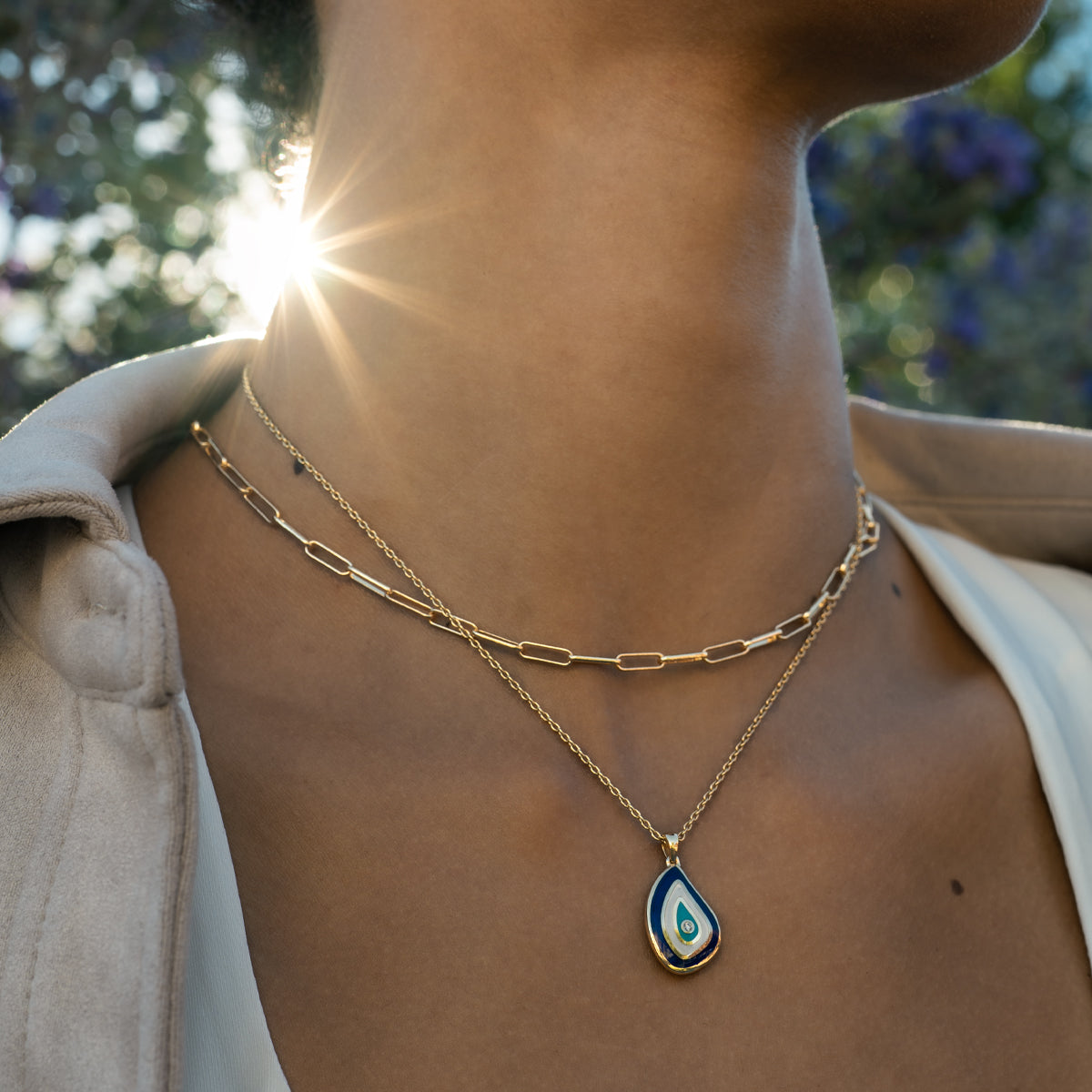 Necklace with a teardrop-shaped evil eye pendant worn by a person in outdoor at the sunset