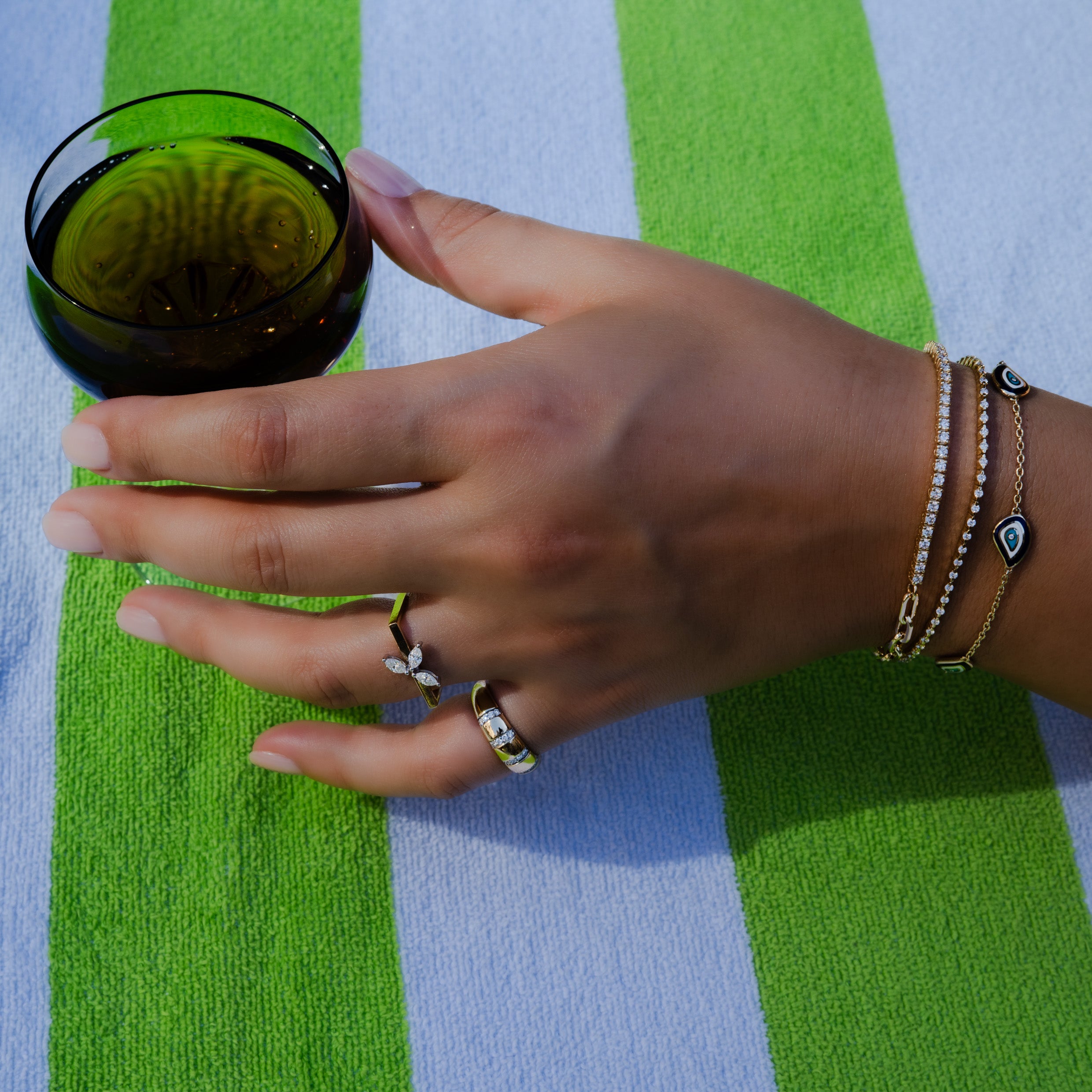 14K gold diamond bracelets and statement rings styled against a green striped beach towel