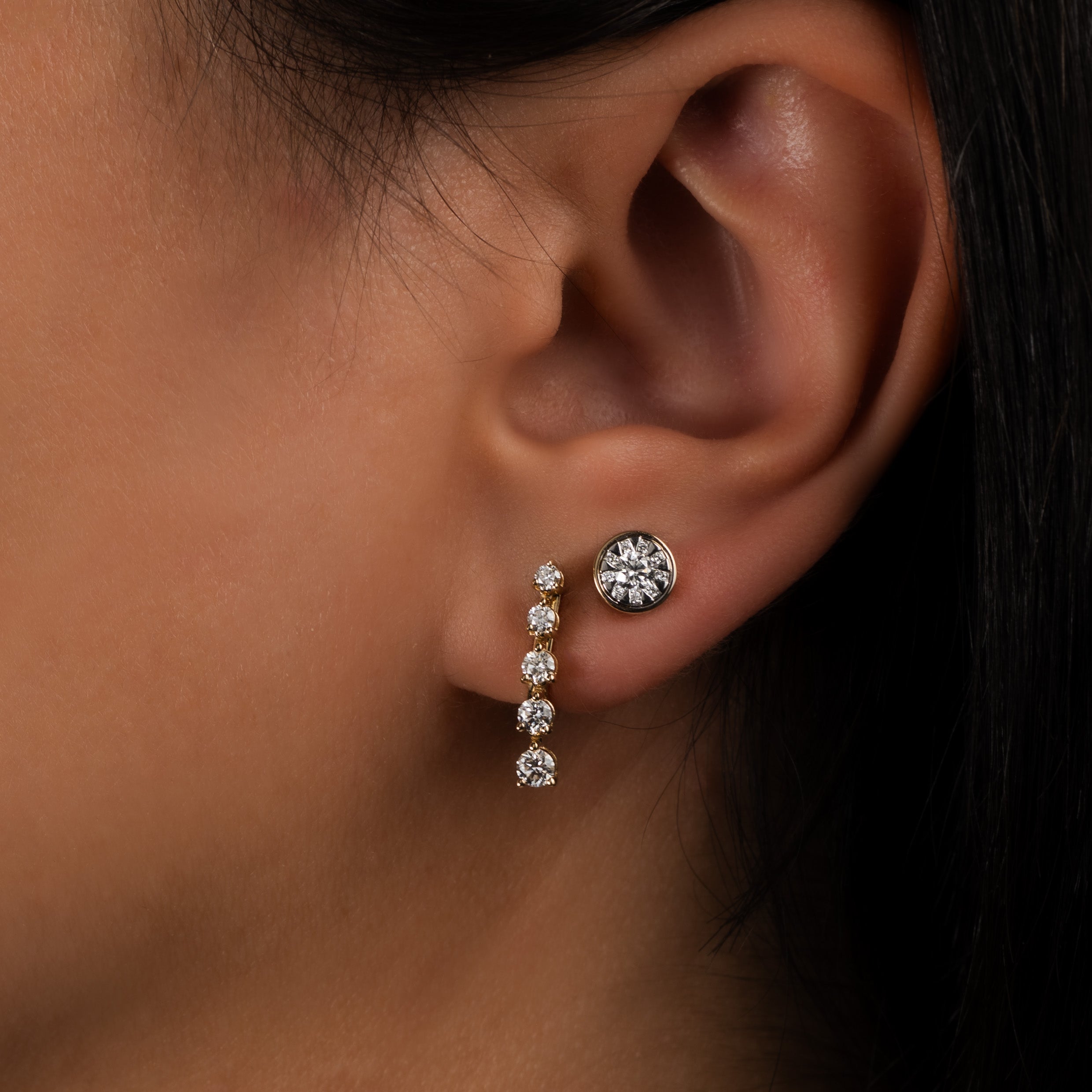 Close-up of an ear featuring a 14K solid gold five-stone diamond drop earring paired with a diamond stud.